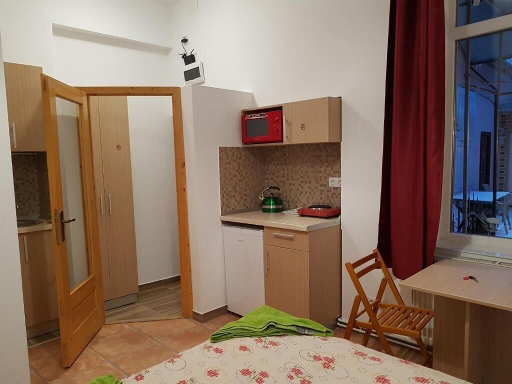 A compact room with a bed, a desk, a chair, a microwave, a small sink, and a window with curtains.
