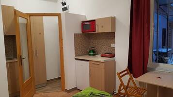 A compact room with a bed, a desk, a chair, a microwave, a small sink, and a window with curtains.
