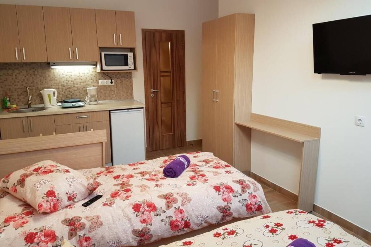 Een kleine kamer met een bed, een kitchenette, een magnetron en een televisie.