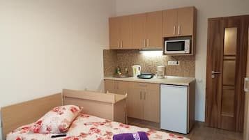 Una habitación pequeña con cama, kitchenette y una puerta.