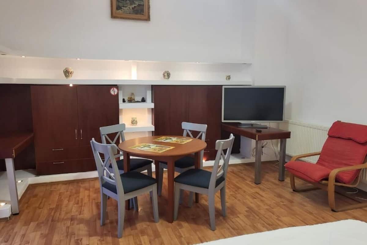 Een kamer met een eettafel, stoelen, een televisie, een rode fauteuil en een bed.