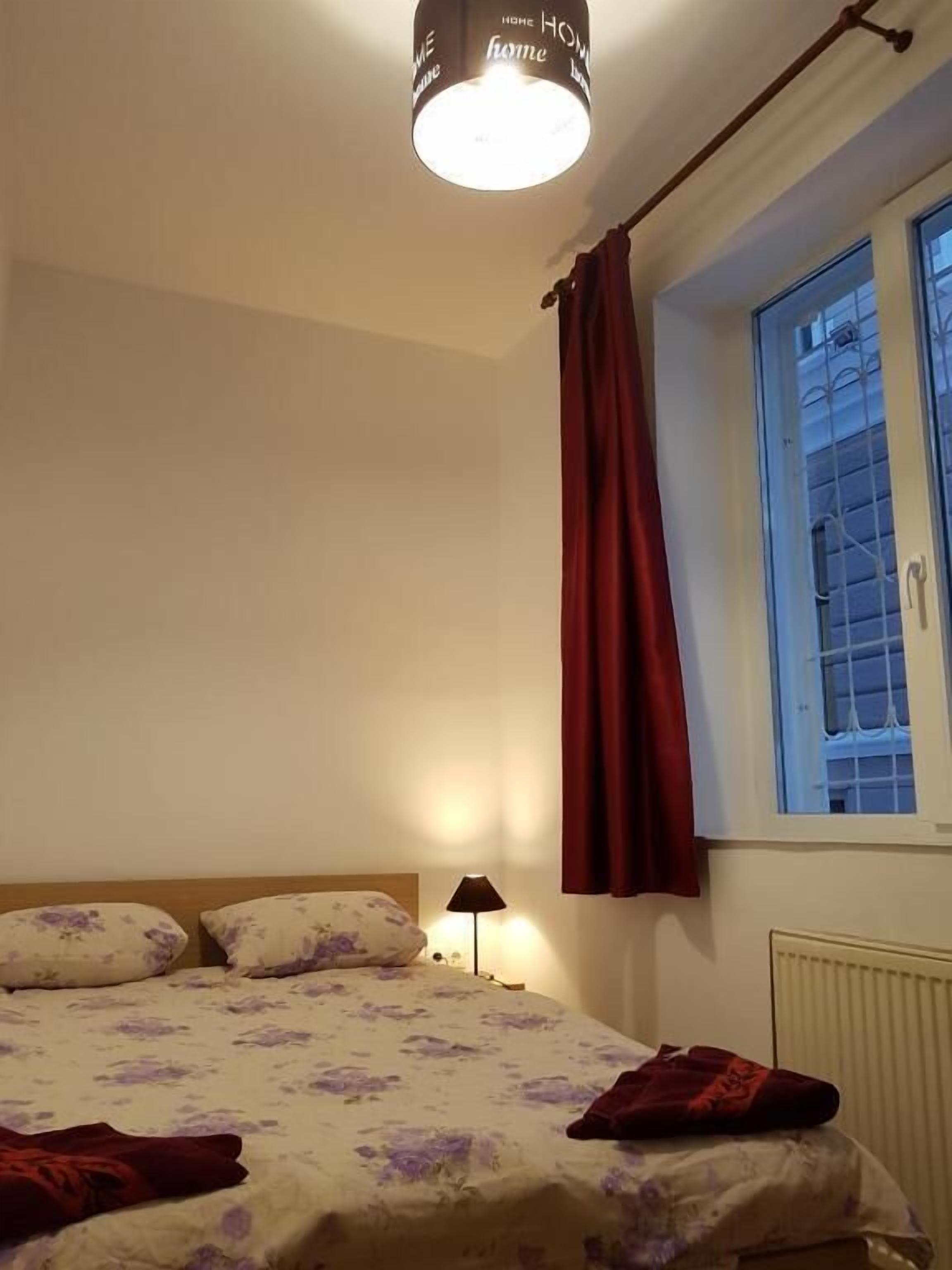 A bedroom with a bed, a window with curtains, a lamp, and a ceiling light fixture.