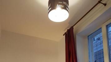 A bedroom with a bed, a window with curtains, a lamp, and a ceiling light fixture.