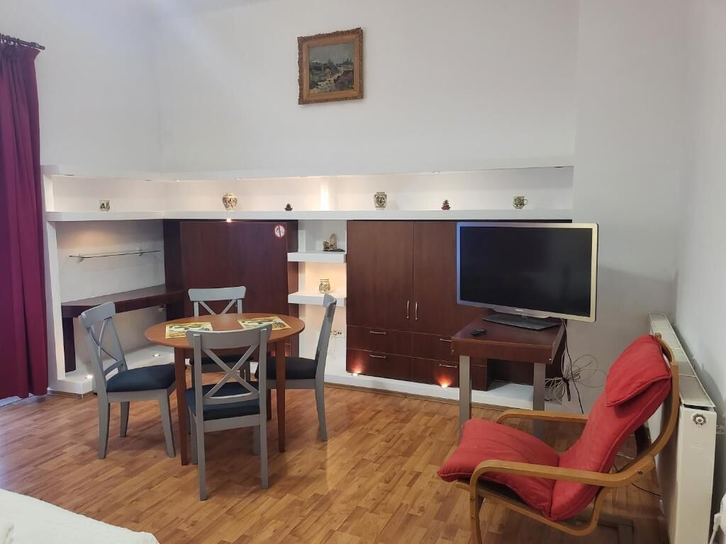 Un ambiente compatto con tavolo, sedie, televisore e una poltrona rossa.