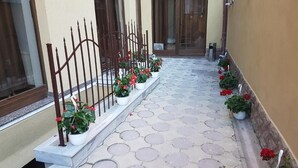 Un camino pavimentado que lleva a la entrada de un edificio, con una valla metálica y macetas.