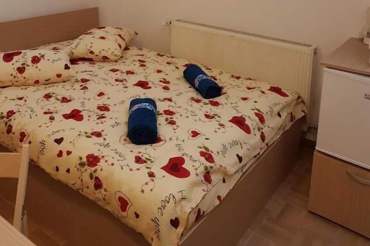 Een slaapkamer met een bed, twee kussens, een radiator, een klein kastje en een dakraam.