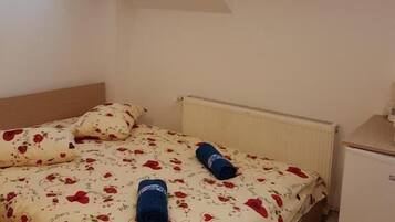 A bedroom with a bed, two pillows, a radiator, a small cabinet, and a skylight.