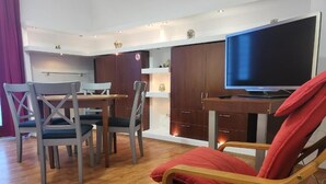 Una sala de estar moderna con una mesa de comedor, sillas, un televisor y armarios de madera.