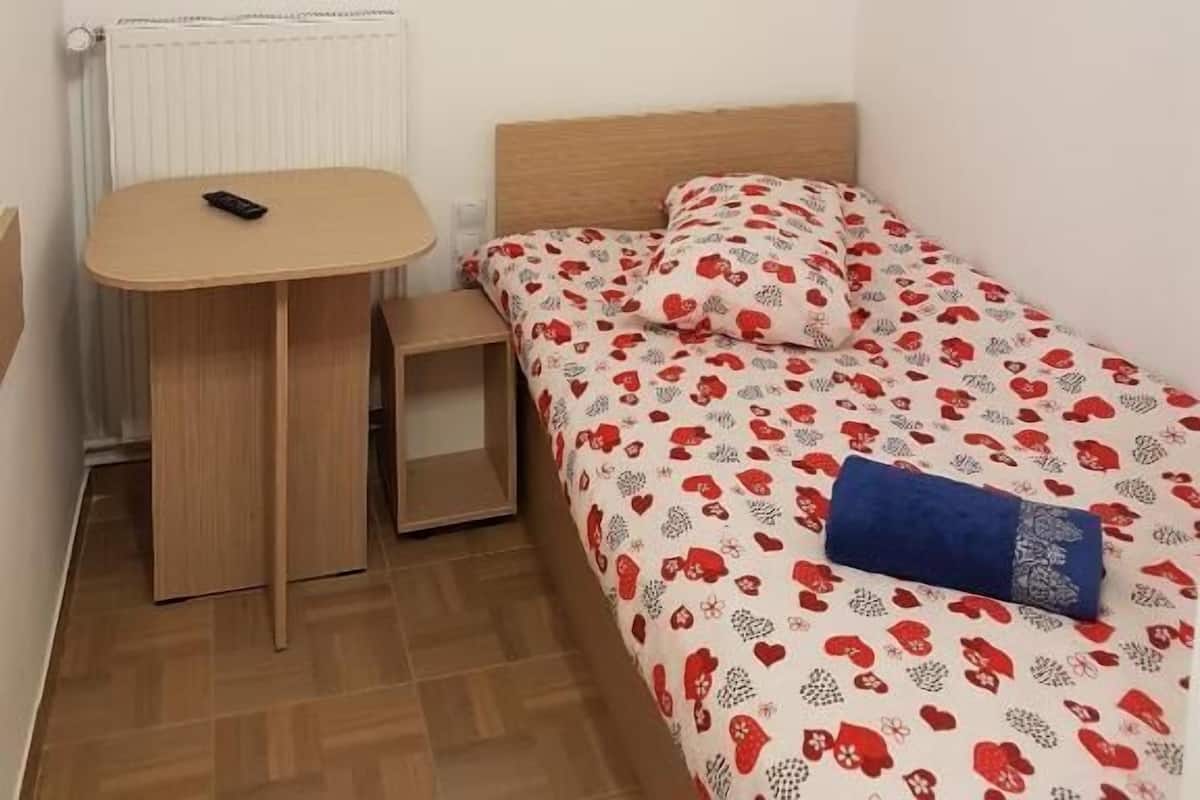 Een kleine kamer met een bed, nachtkastje, lamp en dakraam.