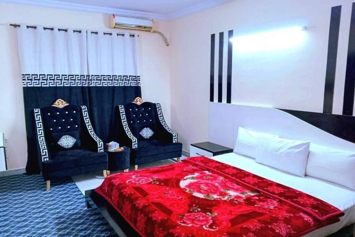 A hotel room with a bed, two armchairs, a small table, a nightstand, and a window with curtains.