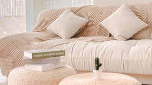 Una cama con una colcha estampada en tonos beige y blanco, dos almohadas y una pequeña planta en una otomana redonda.