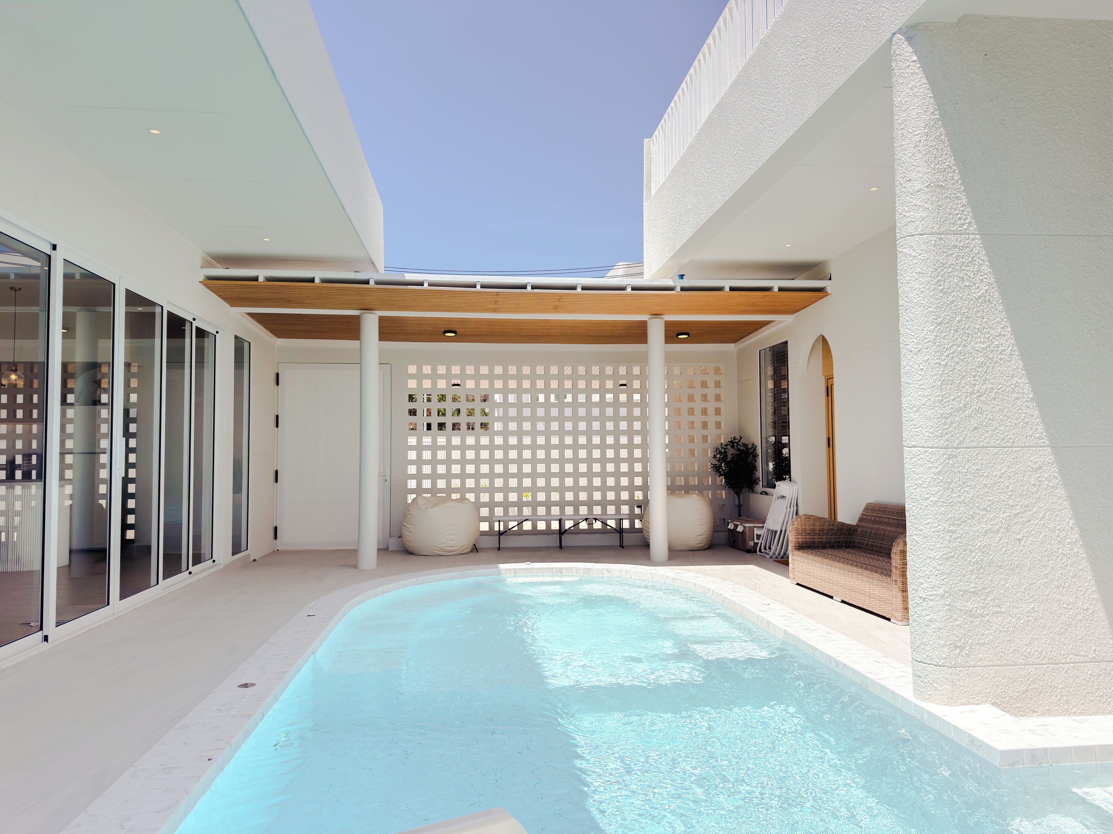 A modern outdoor pool area with a pergola, seating, and a decorative fence.