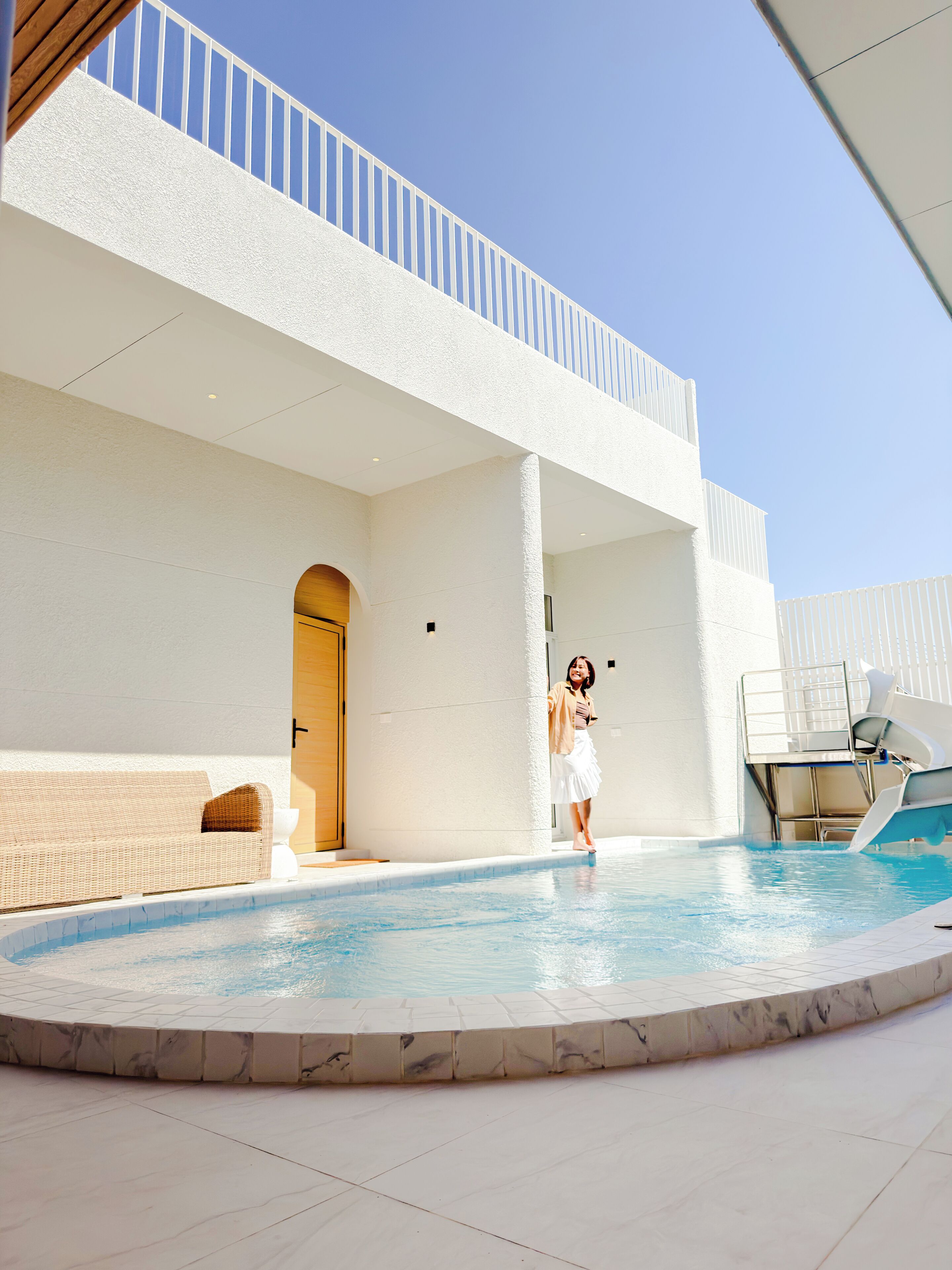 Ein Poolbereich mit weißer Fassade, einer Holztür und einem weißen Stuhl.