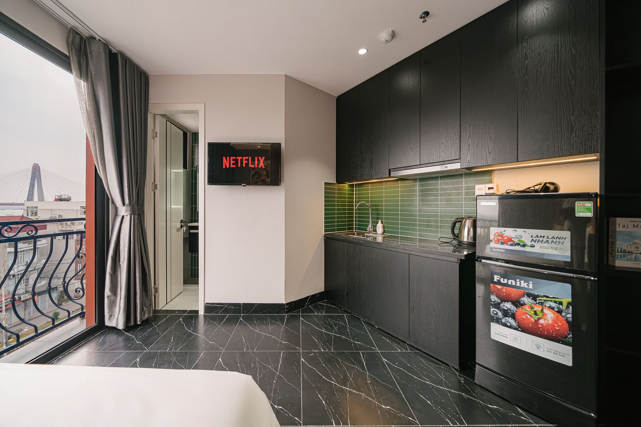 A modern kitchen with a black refrigerator, a wall-mounted TV, and a view of a bridge outside.