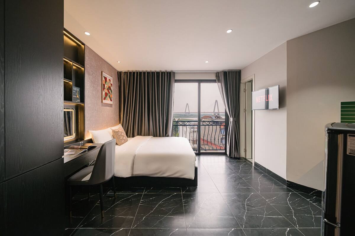 A hotel room with a bed, desk, and chair, a TV, and a balcony with a view.