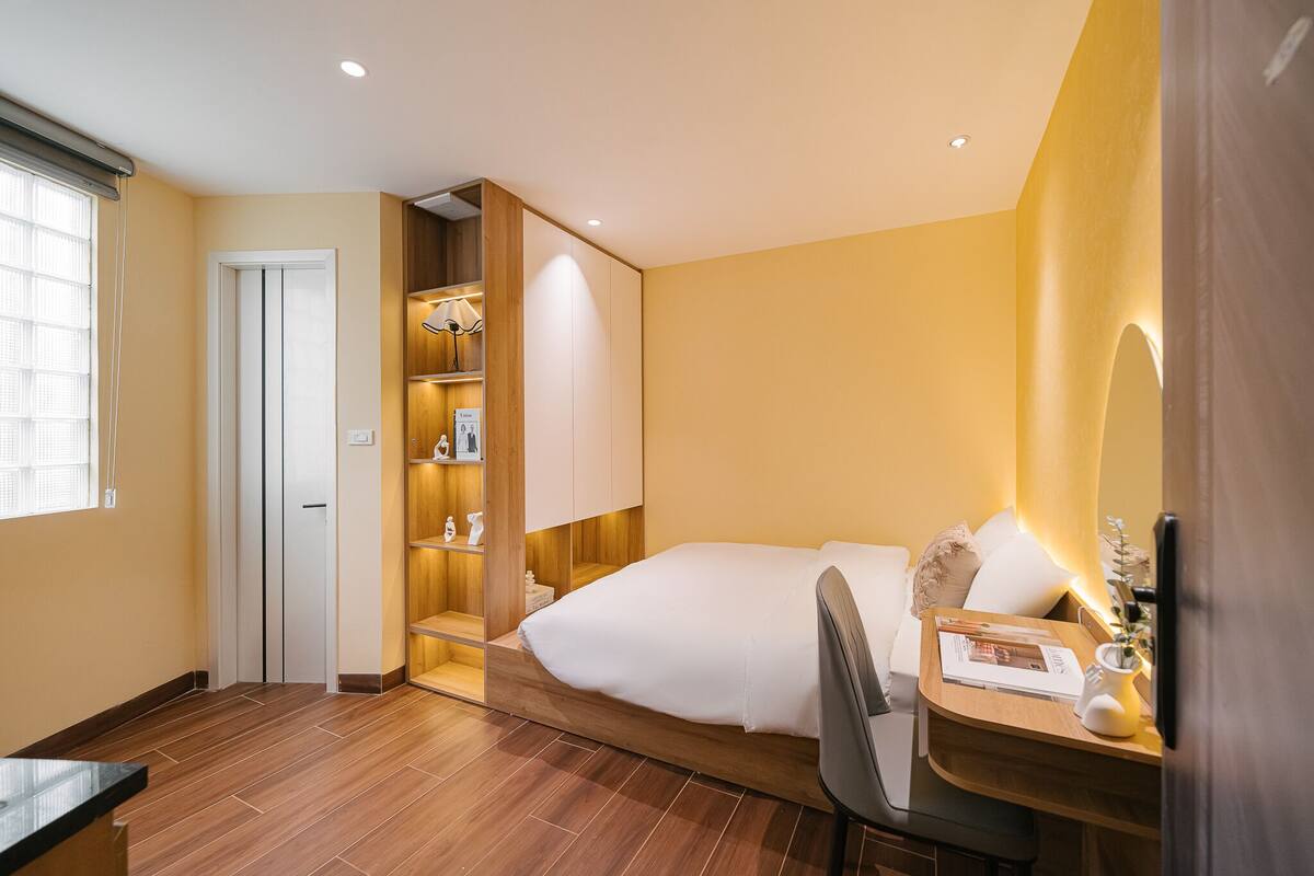 A hotel room with a bed, a desk with a chair, a wardrobe, and a window.