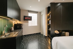 A modern hotel room with a kitchen area, a TV displaying 'NETFLIX,' a window, and a bed. - BOHO Urban Living Westlake (Hanoi)