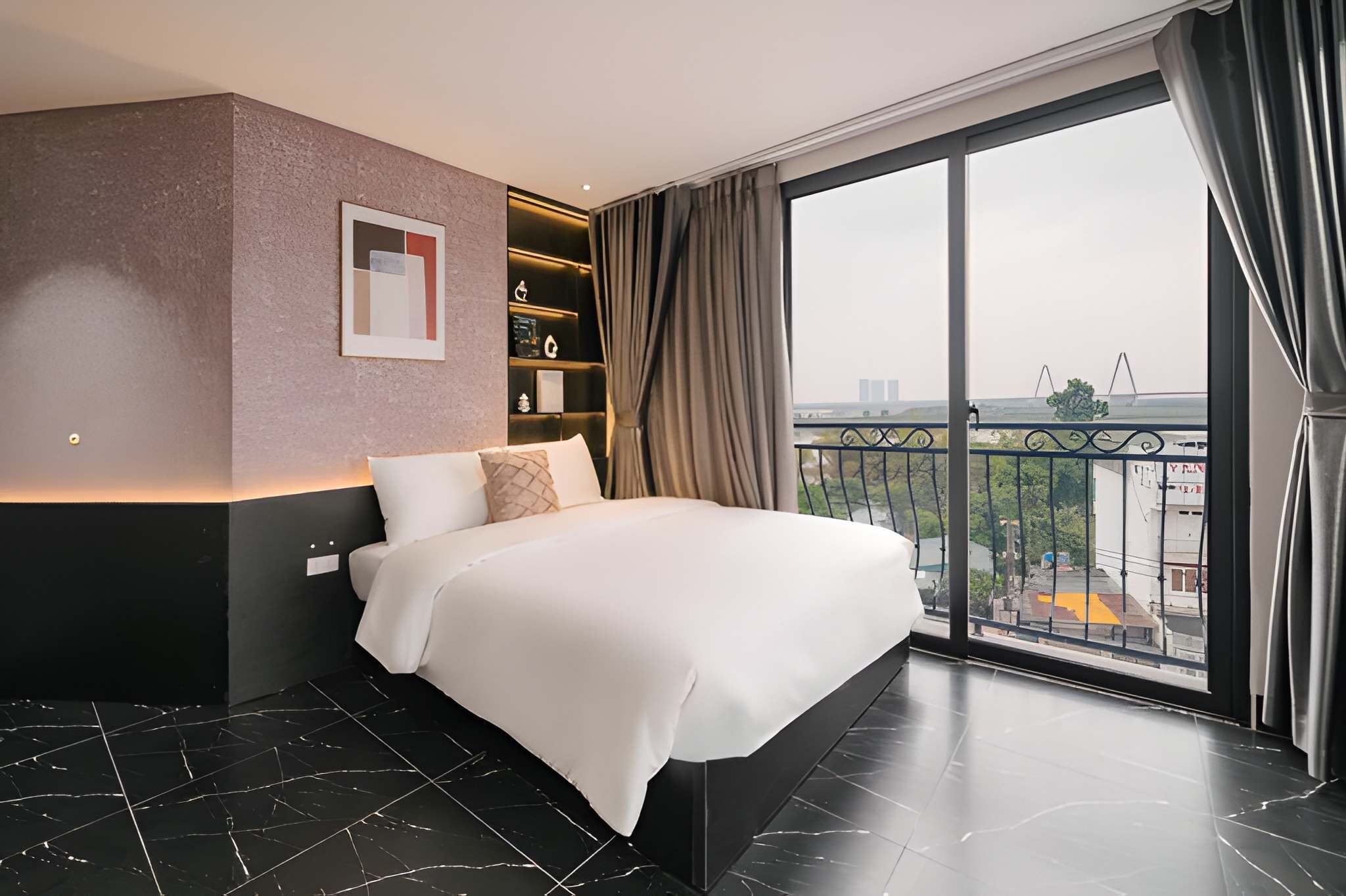 A modern hotel room with a large bed, a built-in shelf with amenities, and a balcony with a city view.