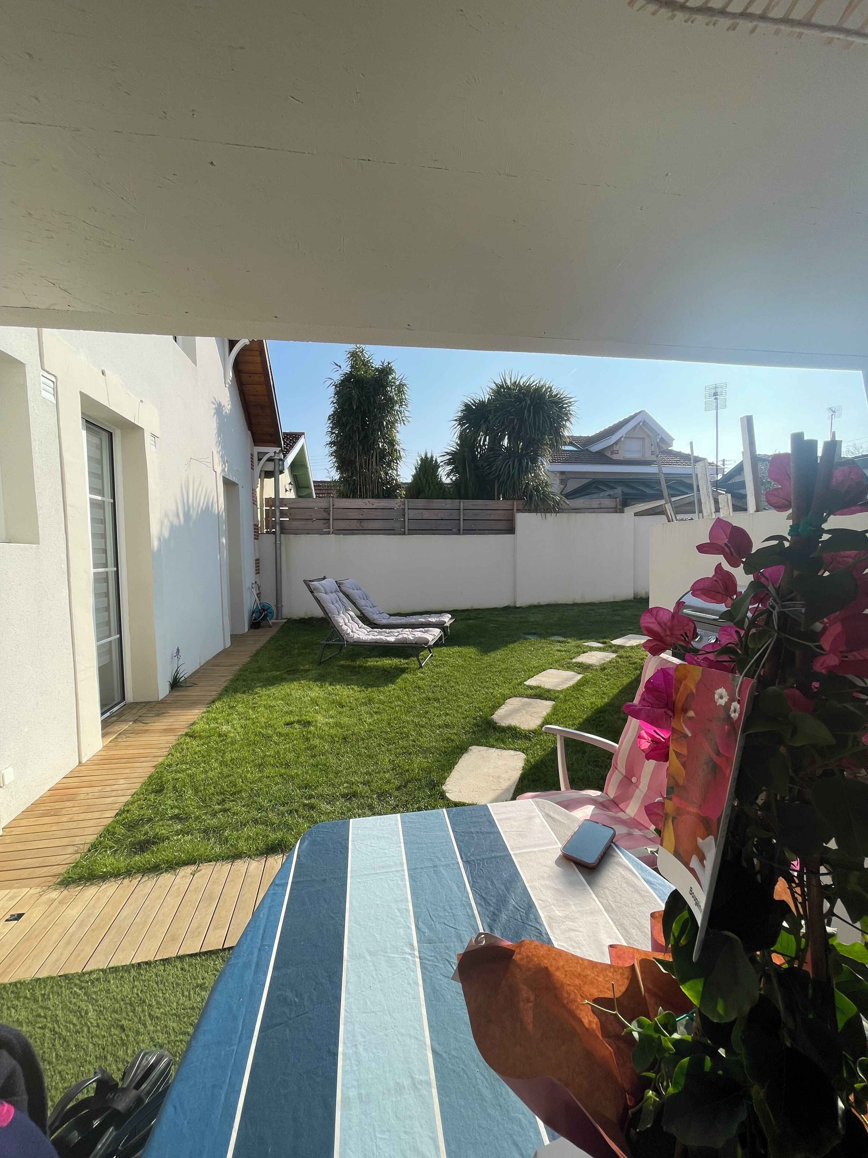 A backyard with a lawn, a wooden deck, a lounge chair, and a potted plant.