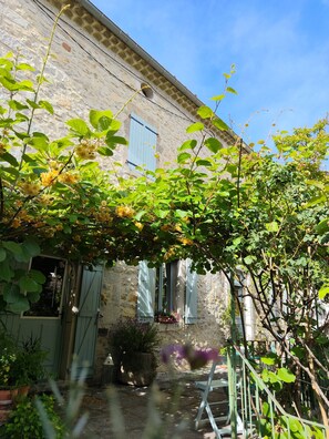 Edifici de pedra amb una finestra i una porta, envoltat de vegetació i una tanca metàl·lica.