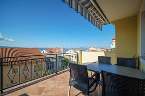 A balcony with a table and chairs, a view of the sea, and buildings in the background. - Comfort apartment for 4 people with balcony and parking space (Crikvenica)