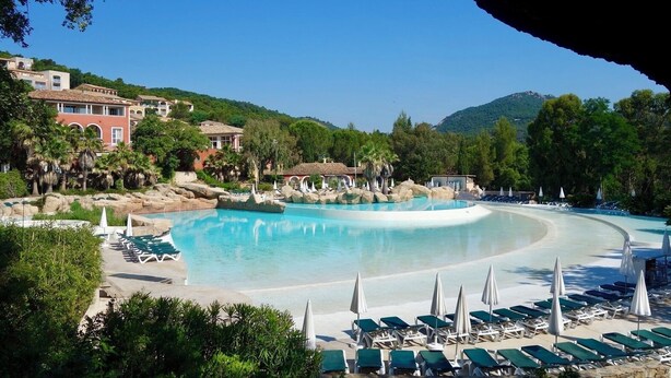 Ett semesterhotell med en stor pool, solstolar och en imponerande bergskedja i bakgrunden.