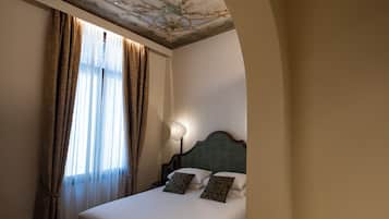 A hotel room with a bed, curtains, a nightstand, and a wall with a decorative ceiling.
