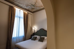Habitación de hotel con cama, cortinas, mesita de noche y un techo decorativo en la pared.