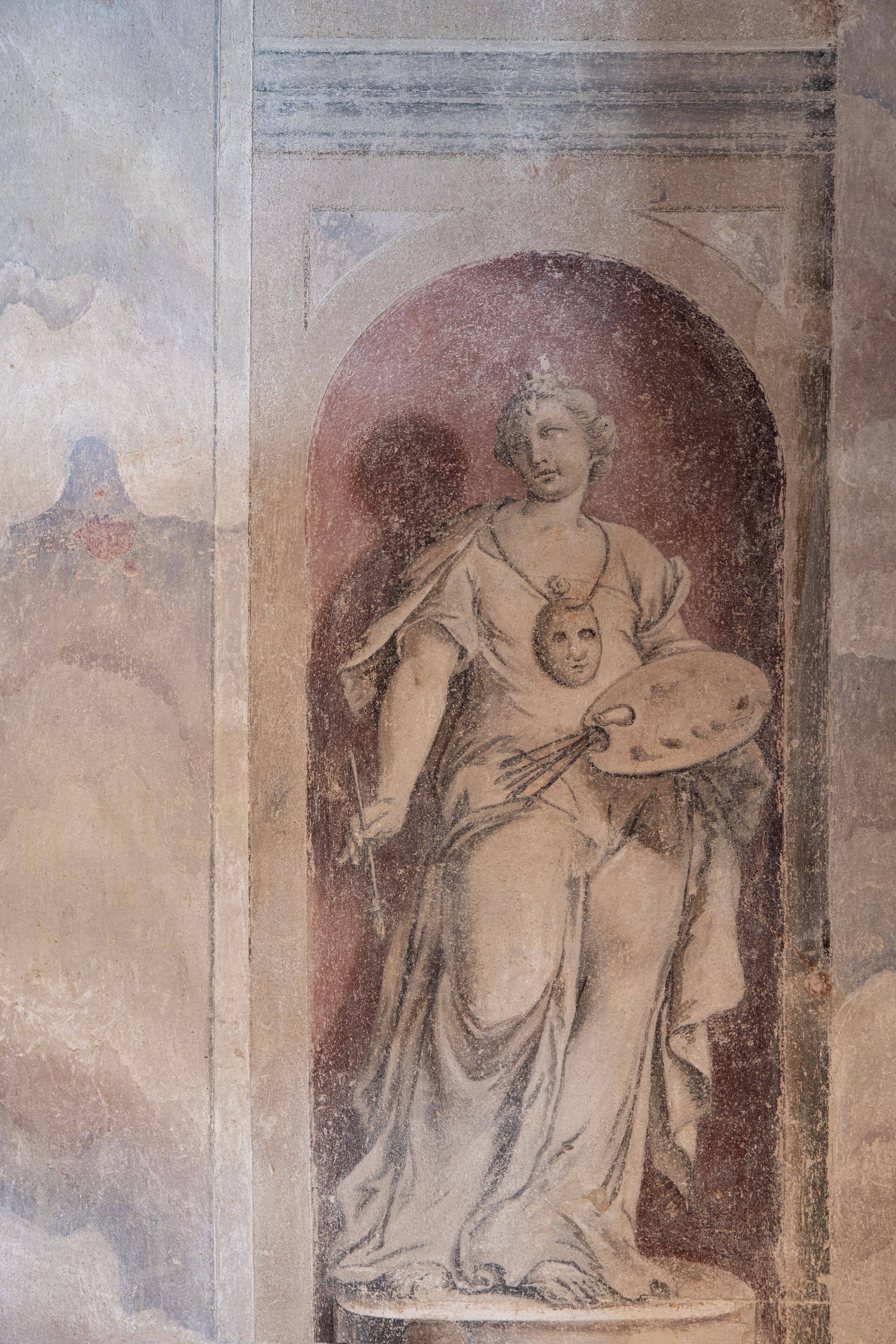 A classical statue with a draped garment, seated on a pedestal, within a niche.