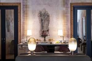 Una habitación con un espejo grande, dos lámparas, una mesa con comida y una escultura de piedra en la pared.