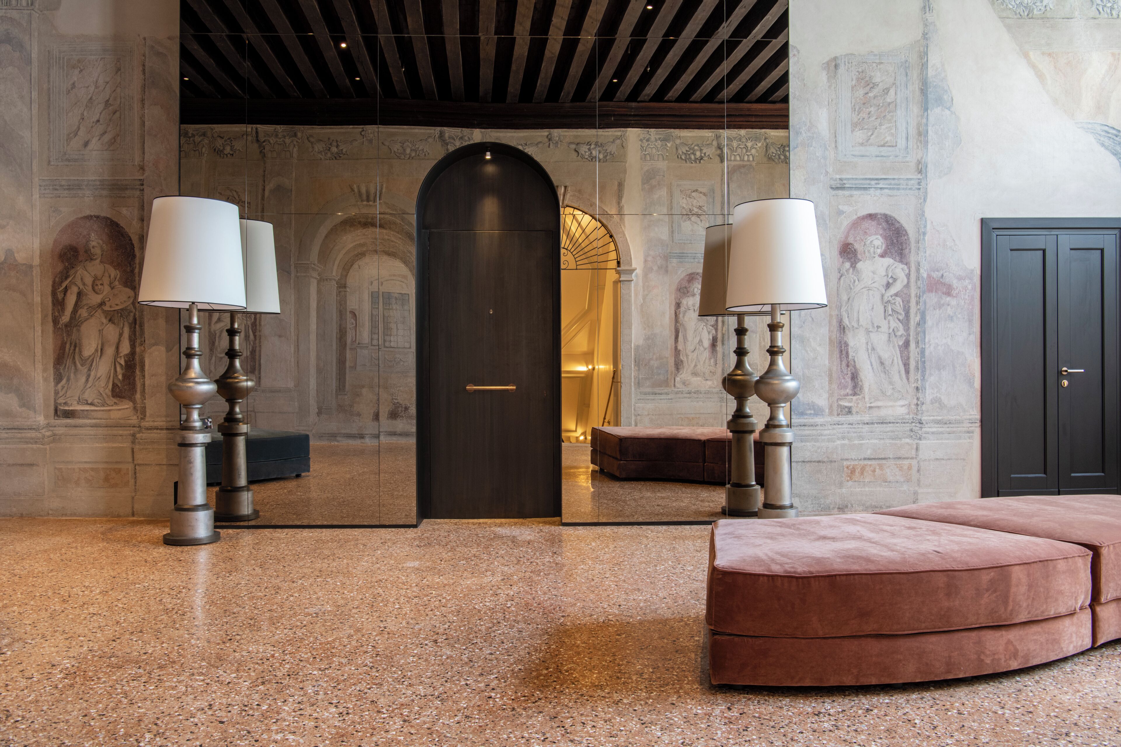 Eine Lobby mit Marmorboden, einer dunklen Holztür und einer Sitzecke mit einer pinkfarbenen Polsterbank.