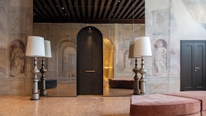 A lobby with a marble floor, a dark wooden door, and a seating area with a pink upholstered bench. - Palazzo De Polo (Venice)