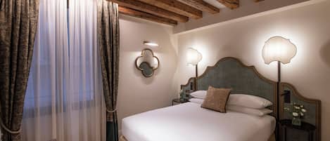 Een hotelkamer met een groot bed, houten balken in het plafond, een nachtkastje met een lamp en een raam met gordijnen.