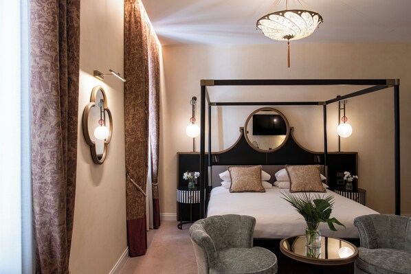 A four-poster bed with a round mirror above it, two bedside tables with lamps, a round coffee table with a vase, and a pair of armchairs. - Palazzo De Polo (Venice)