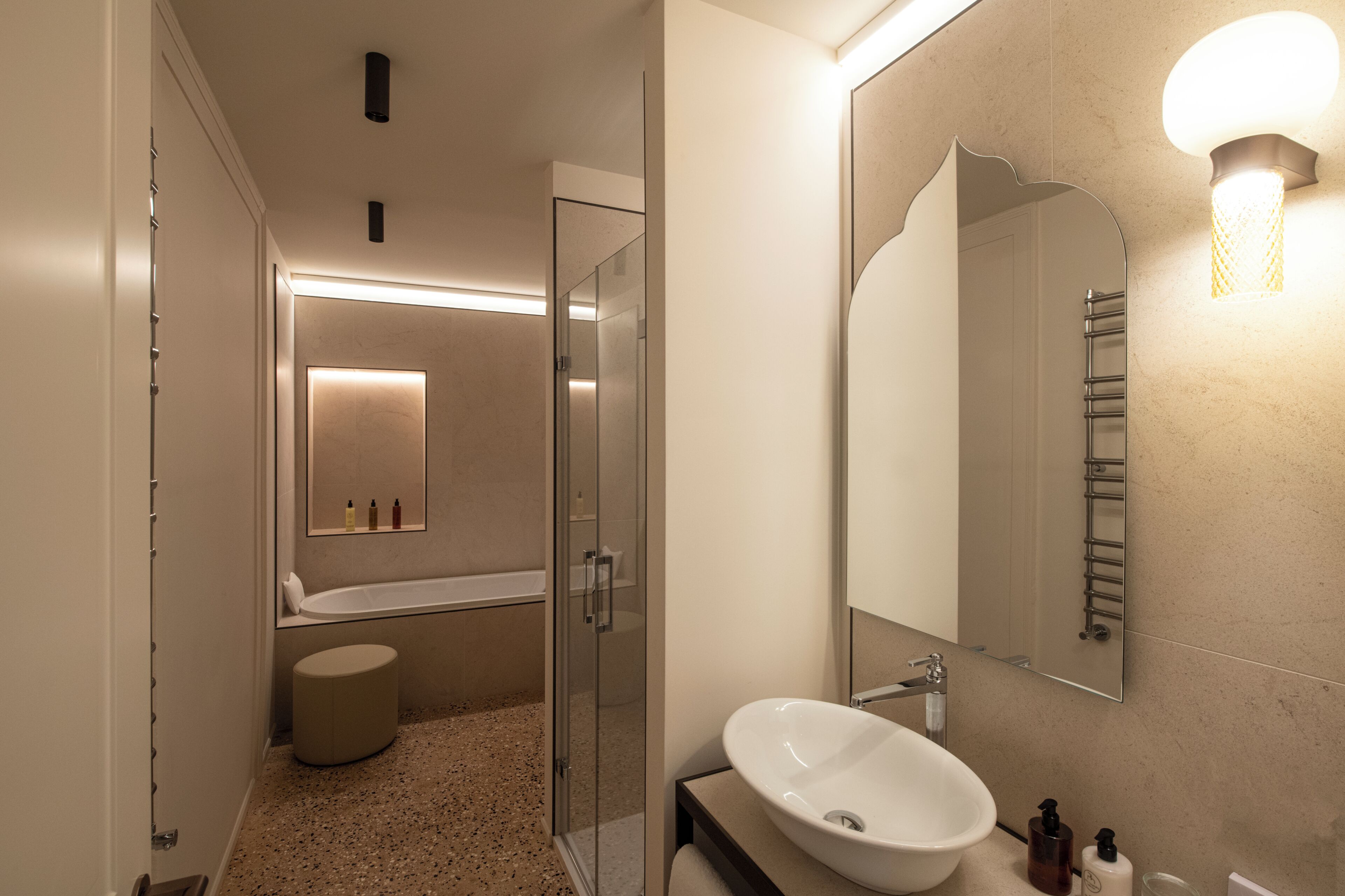 Een moderne badkamer met een vrijstaand bad, een douche met glazen wanden en een grote spiegel met een wandlamp.