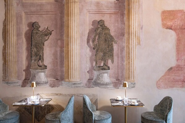 Una habitación con frescos clásicos, una columna de mármol y una mesa con lámpara.