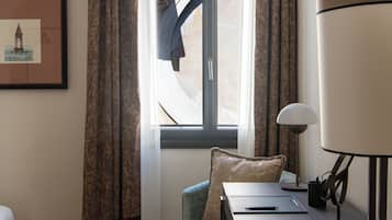 A room with a bed, a desk, a chair, a window with curtains, and a framed picture on the wall.
