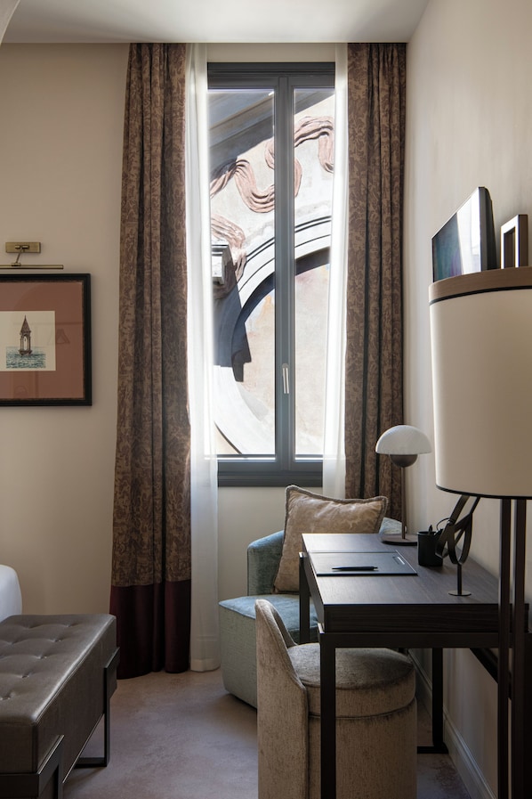 Una habitación con cama, escritorio, silla, ventana con cortinas y un cuadro en la pared.