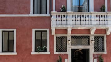 A building with a red facade, multiple windows, a balcony with a balustrade, and potted plants.