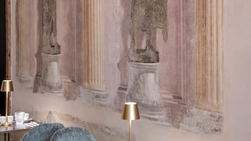 A room with a marble table set for dining, a blue upholstered chair, and a wall with classical statues.