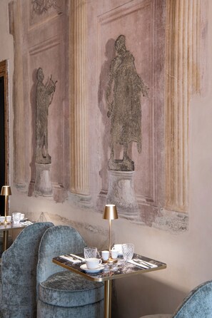 A room with a marble table set for dining, a blue upholstered chair, and a wall with classical statues. - Palazzo De Polo (Venice)