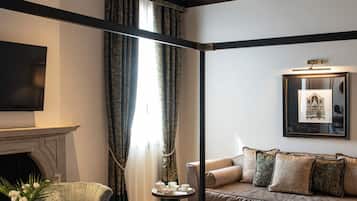 A hotel room with a bed, a sofa, a television, a fireplace, and a chandelier.