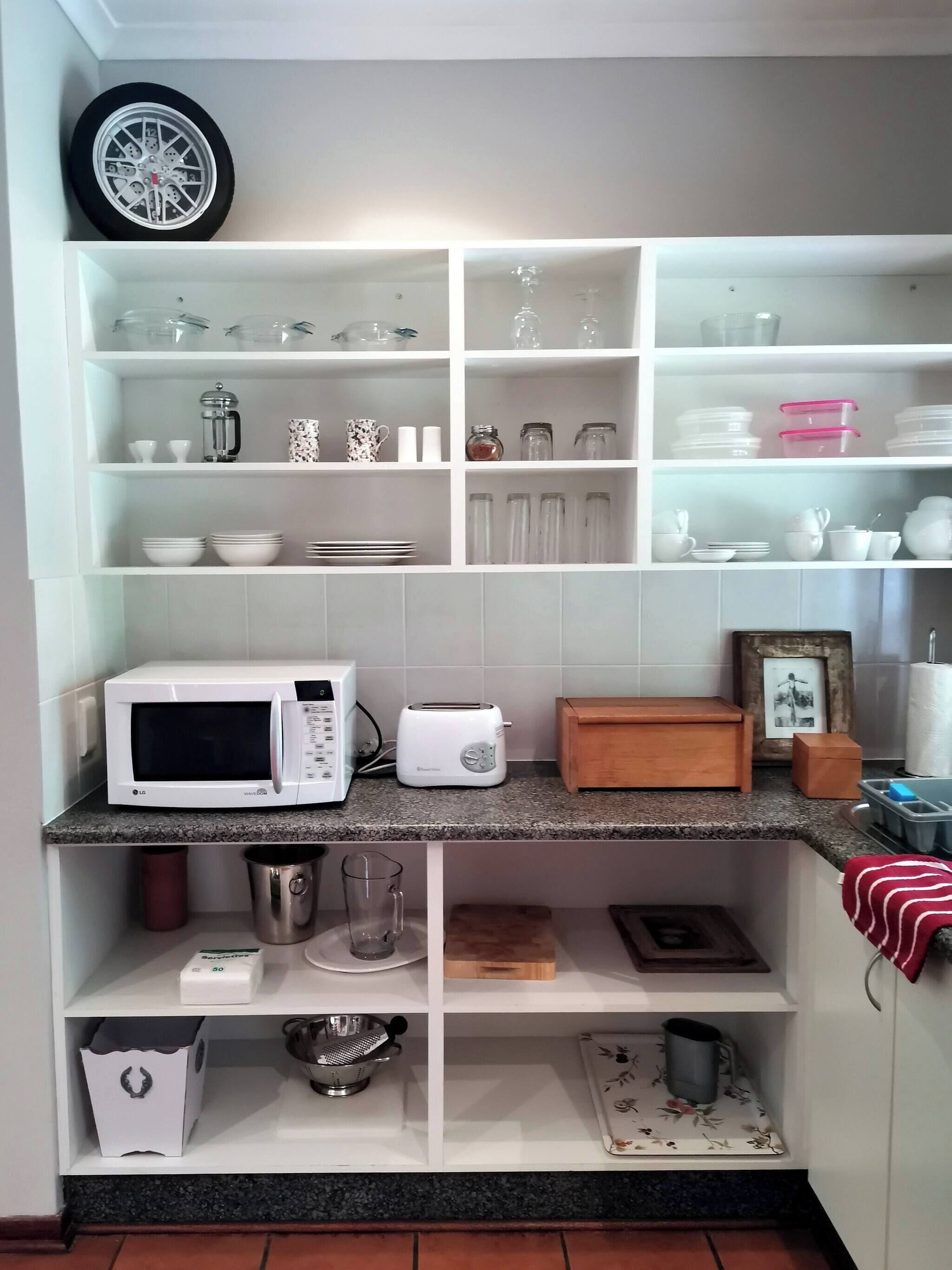 Een keuken met witte kastjes, een magnetron, een broodrooster en diverse keukengerei.