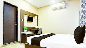 A hotel room with a bed, a desk, a chair, a TV, and an air conditioning unit.