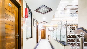 A hotel hallway with wooden doors, a fire extinguisher, a glass railing, and a staircase.