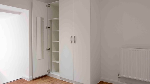 Ein Zimmer mit weißem Kleiderschrank, Heizkörper und Holzboden.