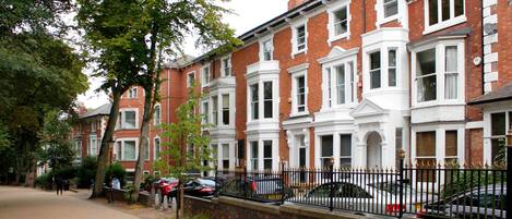 A row of red brick townhouses with white trim, a brick wall, and a black metal fence.