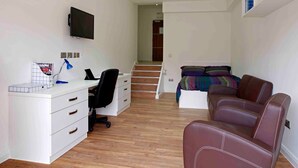 Ein Schlafzimmer mit einem Bett, einem Schreibtisch mit Stuhl, einem Fernseher und einer Treppe, die in einen anderen Raum führt.
