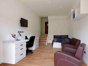 A bedroom with a bed, a desk with a chair, a TV, and a staircase leading to another room. - Student Only 134 New Walk (Leicester)