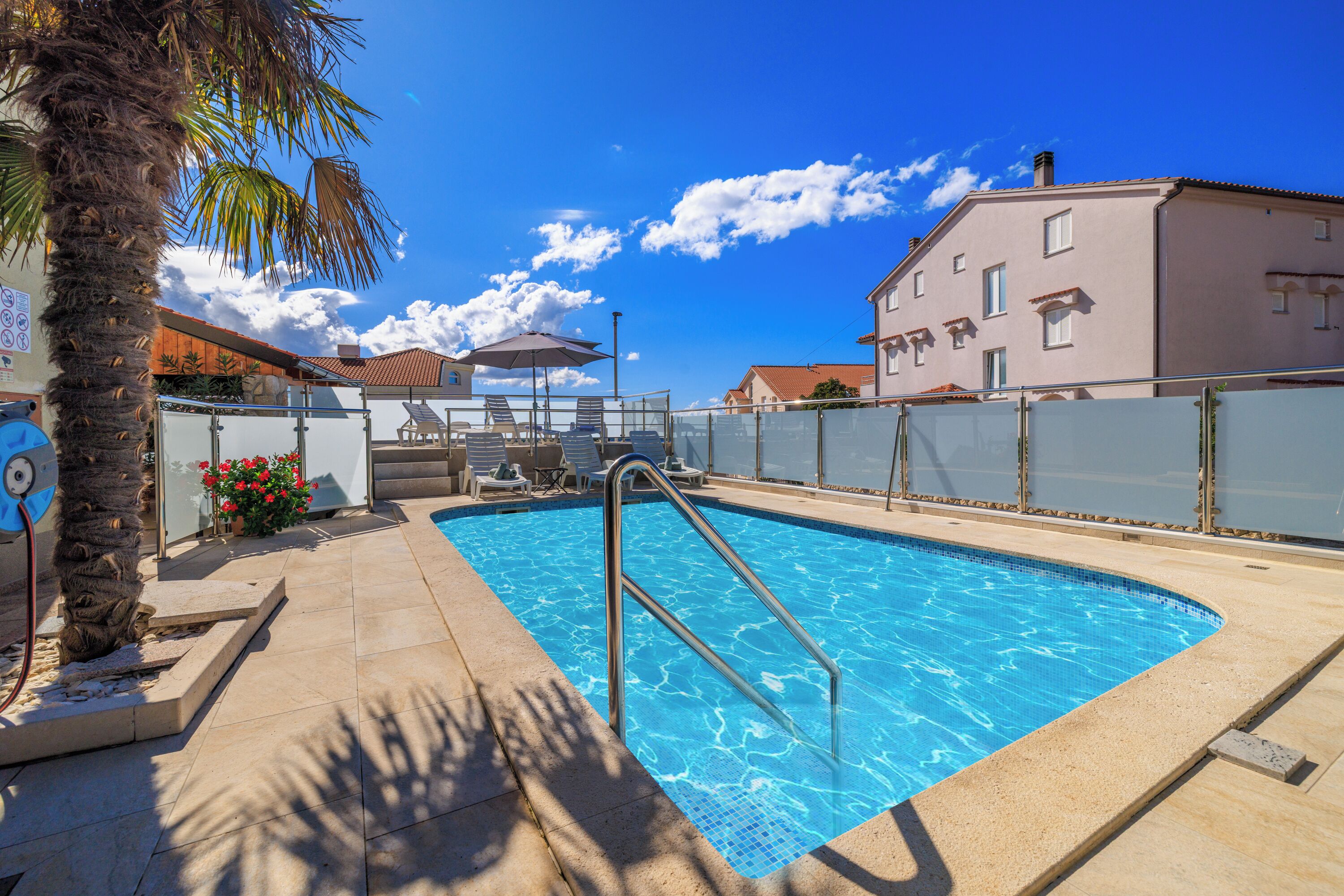 A swimming pool with a metal ladder, lounge chairs, and a palm tree.